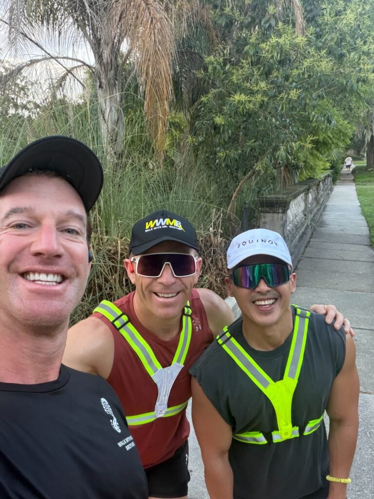 Three men smiling together on a walk, with an arm around a fellow runner’s shoulder.